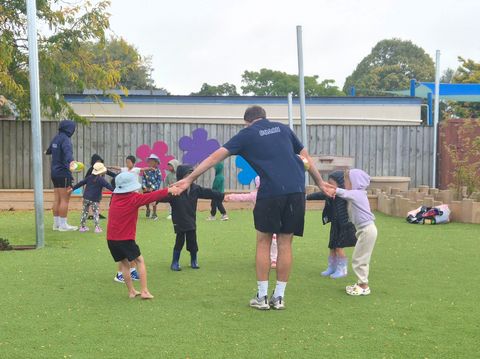Preschool children standing in a circle holding hands with a coach